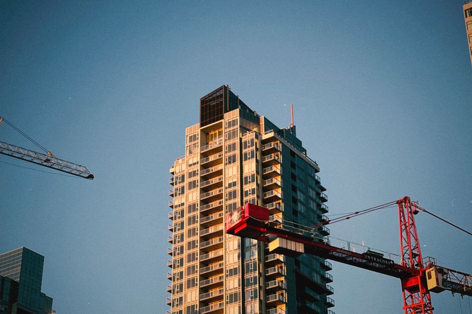 High-rise building with cranes in urban area against blue sky backdrop.