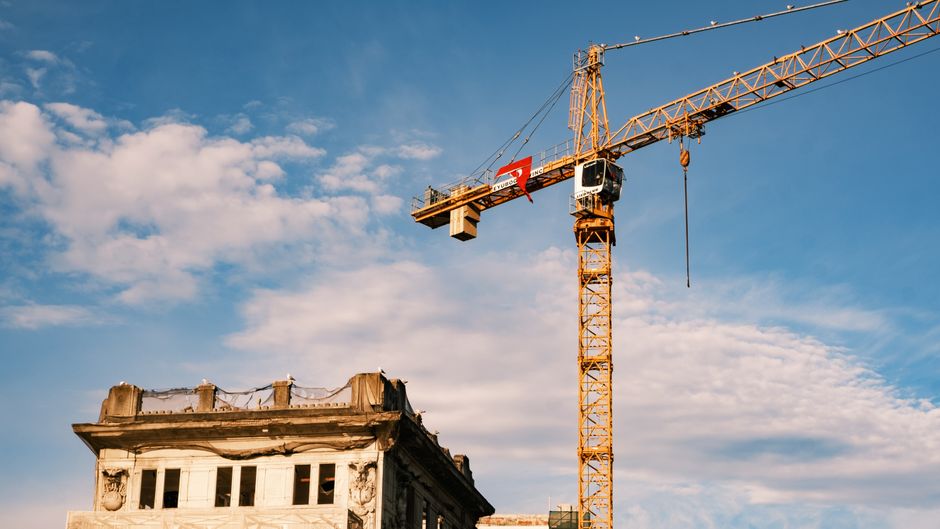 A construction crane towers over a historic building under bright blue skies.