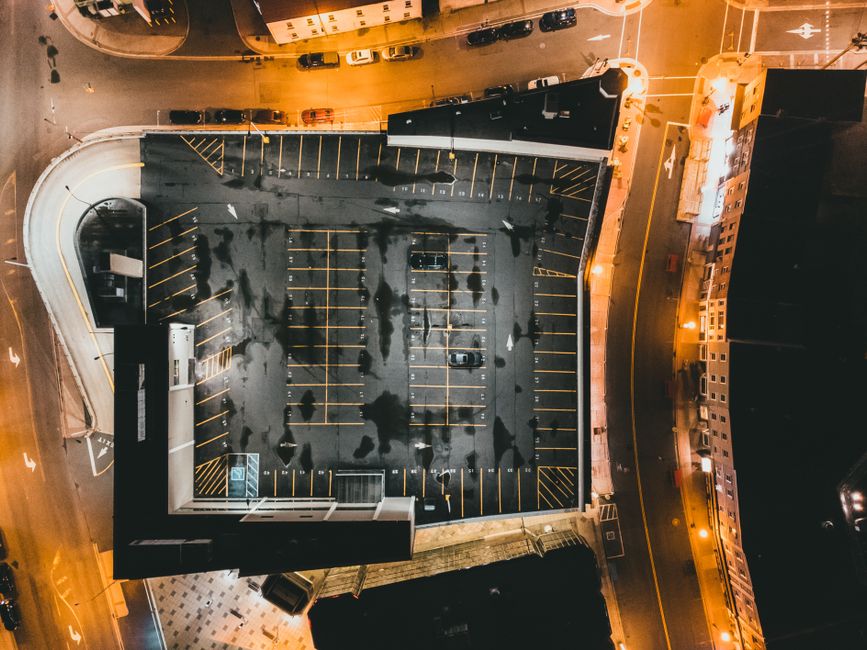 Aerial nighttime view of an urban parking lot surrounded by buildings and roads.