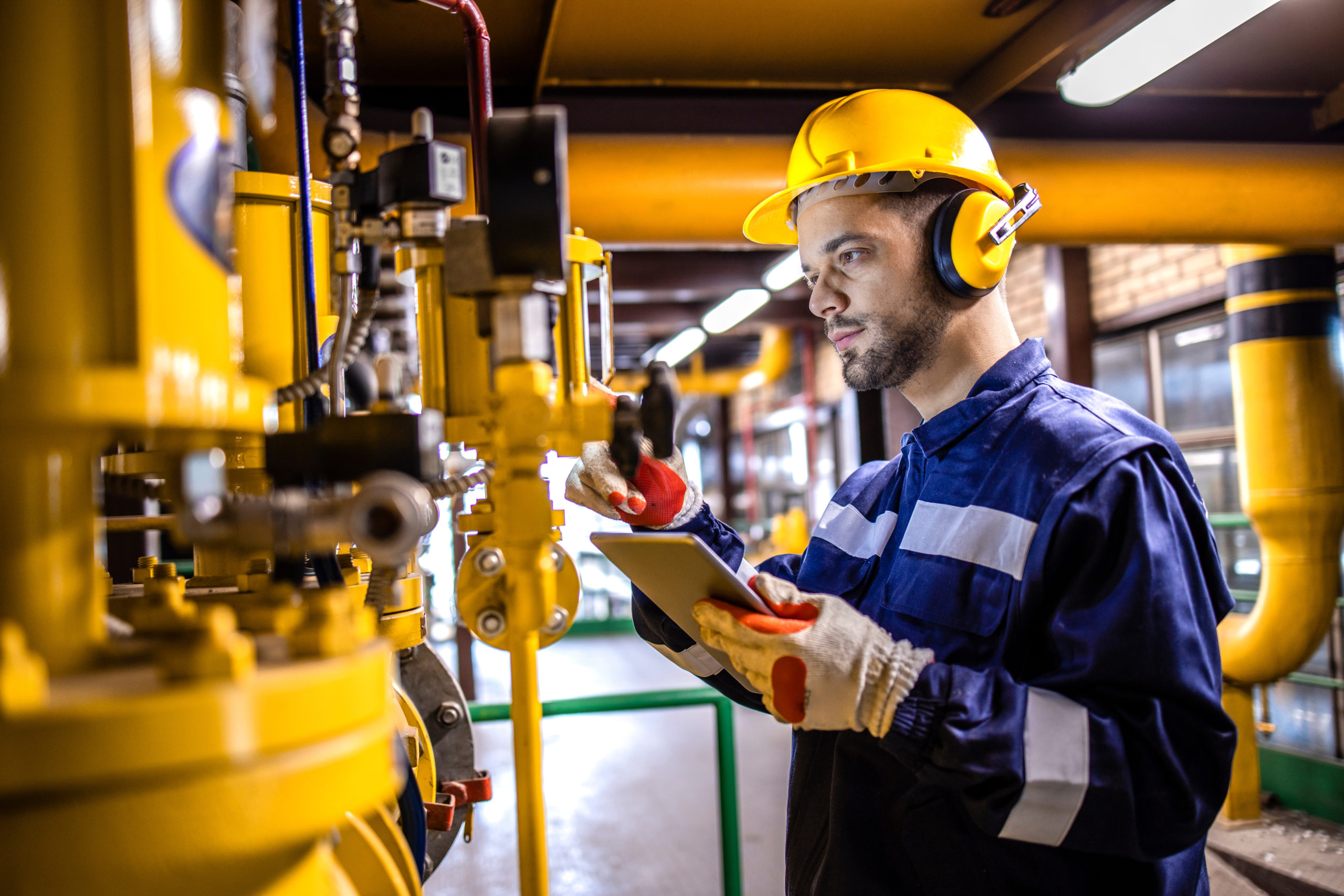 Heating plant technician standing by gas pipes and maintaining temperature inside power plant boiler room.