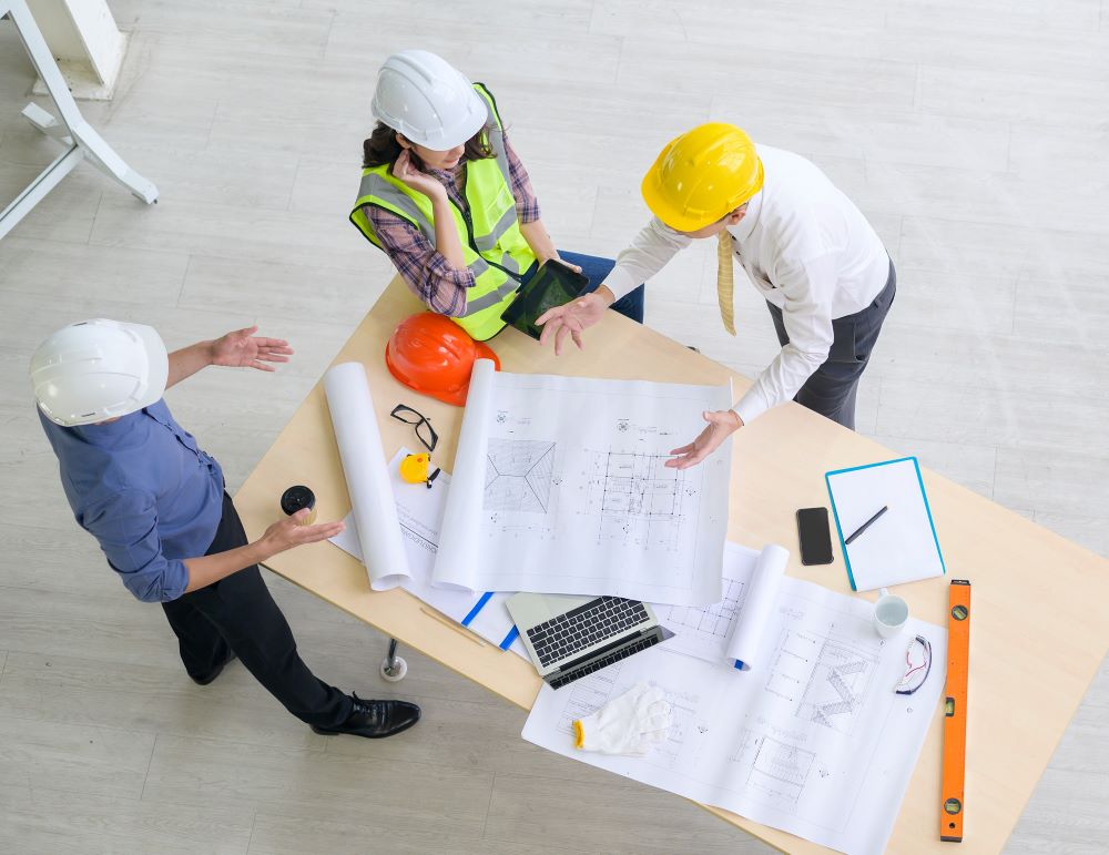 Three individuals in hardhats looking over blueprints