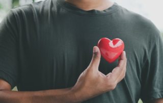 man holding a red heart over his heart to show it is healthy
