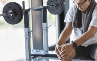 older man sitting on weight bench holding his knee in pain