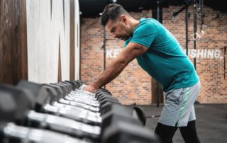man leaning sluggishly on a dumbbell rack