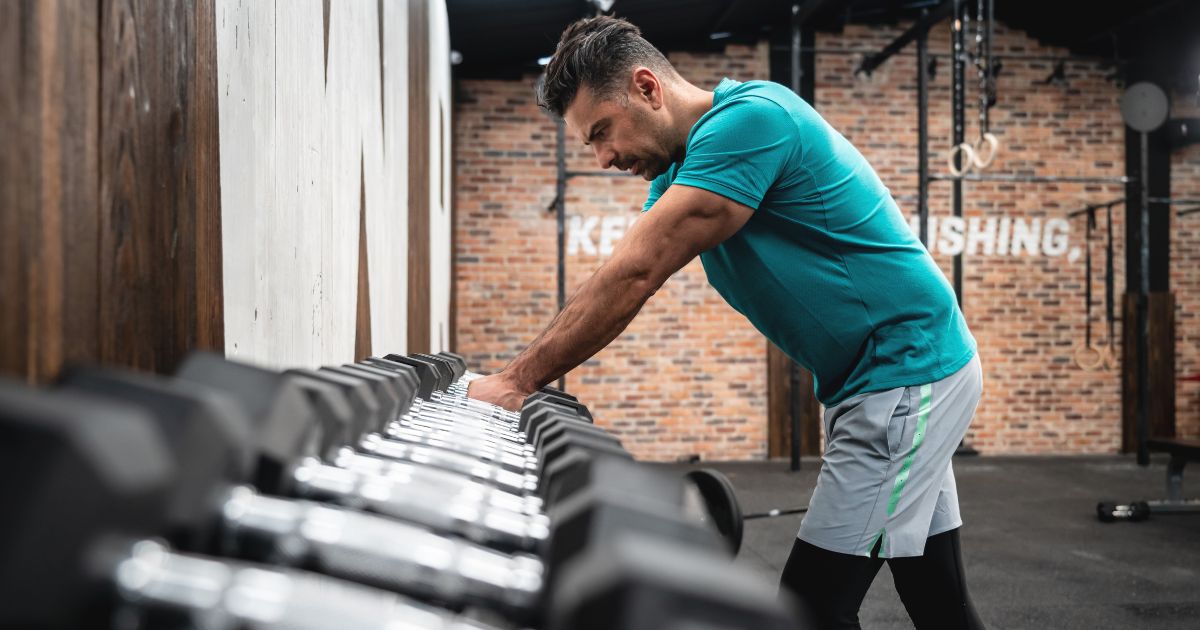 man leaning sluggishly on a dumbbell rack
