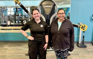 Personal trainer and client smiling together at Westlake Recreation Center in front of gym equipment.