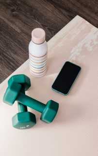 Green dumbbells, a smartphone, and a striped water bottle on a pink yoga mat.