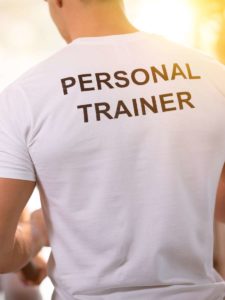 Back view of a male personal trainer wearing a white shirt with “Personal Trainer” printed in bold black letters.