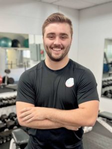 Mason Cover, personal trainer at Prescription Fitness and Butler Fitness, standing in the gym with arms crossed and smiling.