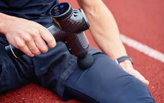 Person using a massage gun on their thigh while sitting on a track.