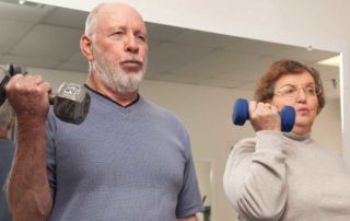 Older man and woman lifting dumbbells together during a workout at the gym.