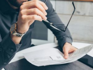 Person looking at papers with glasses in hand
