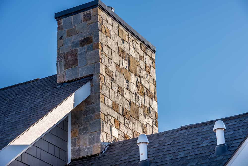 Large Stone Cladding covered masonry chimney on top of a asphalt